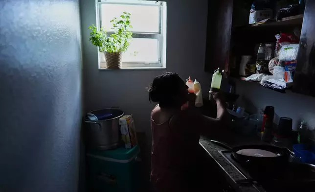 Guatemalan migrant Amavilia, 31, gets out the sauces she uses to flavor the corn on the cob she sells, inside her South Florida apartment, Wednesday, Oct. 8, 2025, after her infant son's father, who worked in construction, was detained and deported to Guatemala. (AP Photo/Rebecca Blackwell)