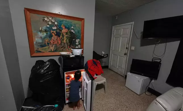 The two-year-old son of pregnant, asylum-seeker Yaoska hunts for a snack in the mini fridge of the Miami-area motel room where he lives with his mother and brother, after their father was deported to Nicaragua, Thursday, Nov. 13, 2025. (AP Photo/Rebecca Blackwell)