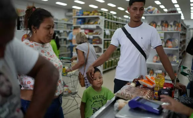 Mariela Gómez, her partner Abraham Castro, and her son Mathias, a Venezuelan migrant family who abandoned their journey to the United States and returned home following President Donald Trump's immigration crackdown, buy groceries for Christmas dinner in Maracay, Venezuela, Wednesday, Dec. 24, 2025. (AP Photo/Matias Delacroix)