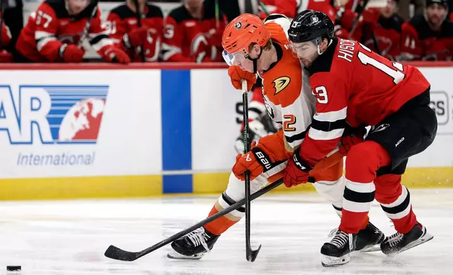 Anaheim Ducks defenseman Jackson Lacombe (2) battles for the puck with New Jersey Devils center Nico Hischier (13) during the second period of an NHL hockey game Saturday, Dec. 13, 2025, in Newark, N.J. (AP Photo/Adam Hunger)