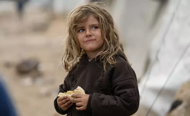 A young girl looks on as she holds a sandwich at a tent camp for displaced Palestinians on the beach in Gaza City Wednesday, Dec. 10, 2025. (AP Photo/Jehad Alshrafi)
