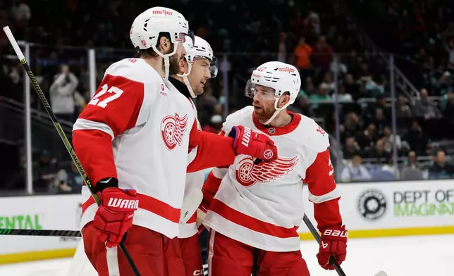 Detroit Red Wings left wing James van Riemsdyk (21), center, celebrates a goal with center Michael Rasmussen (27) and left wing J.T. Compher, right, against the Seattle Kraken during the second period of an NHL hockey game Saturday, Dec. 6, 2025, in Seattle. (AP Photo/John Froschauer)