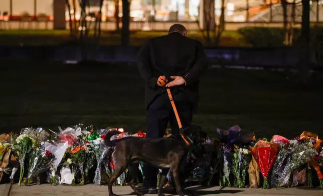 A man walks a dog close to a memorial near Brown University's Barus and Holley building in Providence, R.I., Wednesday, Dec. 17, 2025. (Lily Speredelozzi/The Sun Chronicle via AP)