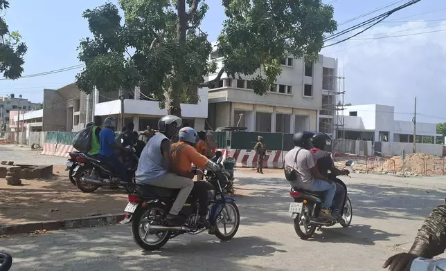 People on motorcycles pass by soldiers guarding a street amid an attempted coup in Cotonou Benin, Sunday Dec. 7, 2025. (AP Photo)