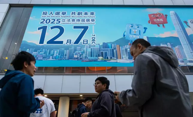 Pedestrians walk past the banner promoting the Hong Kong Legislative Council General Election in Hong Kong on Wednesday, Dec. 3, 2025. (AP Photo/Chan Long Hei)