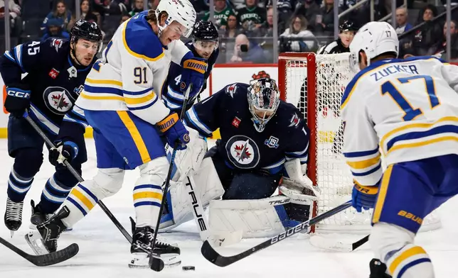 Winnipeg Jets goaltender Eric Comrie (1) keeps his eye on the rebound as Buffalo Sabres' Josh Doan (91) tries to knock it in during first period NHL action in Winnipeg on Friday, Dec. 5, 2025. (John Woods/The Canadian Press via AP)