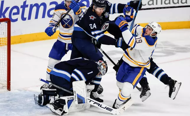 Winnipeg Jets' Logan Stanley (64) clears Buffalo Sabres' Peyton Krebs (19) from in front of goaltender Eric Comrie (1) during the second period of an NHL hockey game, in Winnipeg, Manitoba, Friday, Dec. 5, 2025. (John Woods/The Canadian Press via AP)