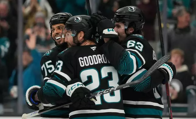 San Jose Sharks center Barclay Goodrow, middle, is congratulated by right wing Ryan Reaves (75) and center Zack Ostapchuk (63) after scoring against the Calgary Flames during the first period of an NHL hockey game in San Jose, Calif., Tuesday, Dec. 16, 2025. (AP Photo/Jeff Chiu)