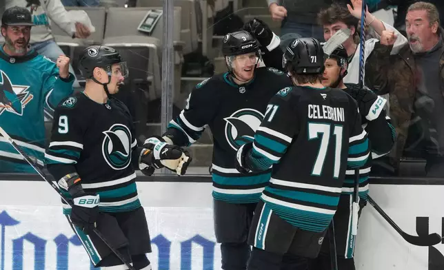 San Jose Sharks defenseman John Klingberg, middle, is congratulated by defenseman Dmitry Orlov (9), center Macklin Celebrini (71) and left wing Jeff Skinner after scoring against the Calgary Flames during the first period of an NHL hockey game in San Jose, Calif., Tuesday, Dec. 16, 2025. (AP Photo/Jeff Chiu)