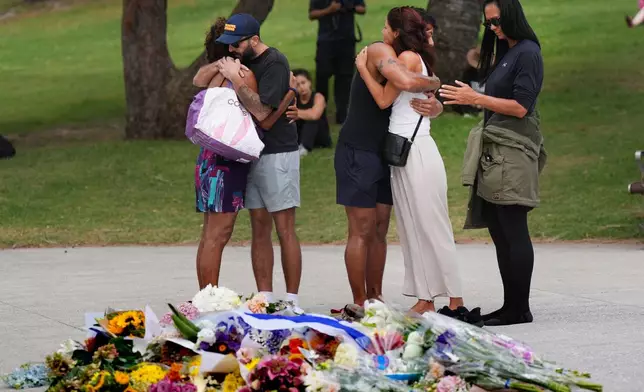 People embrace at a flower memorial placed outside Bondi Pavilion at Sydney's Bondi Beach, Monday, Dec. 15, 2025, a day after two gunmen opened fire during a Hanukkah celebration. (AP Photo/Mark Baker)
