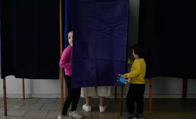 Children wait for their mother to mark the ballot during the presidential runoff election in Santiago, Chile, Sunday, Dec. 14, 2025. (AP Photo/Matias Delacroix)