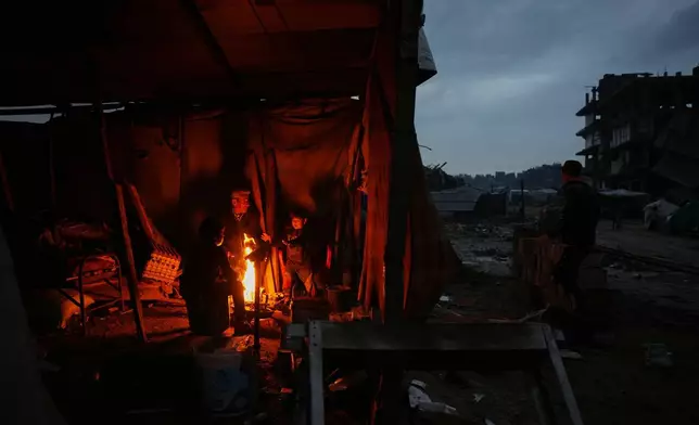 Aziz Halawa, 60, sits with his children as they warm themselves next to the fire inside their tent amid the destruction left by the Israeli air and ground operations in Gaza City, Friday, Dec. 12, 2025. (AP Photo/Abdel Kareem Hana)