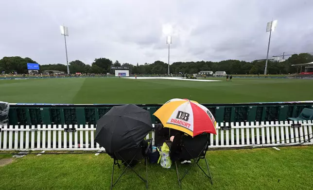 Fans wait under umbrellas during a during a rain delay during the cricket test match between New Zealand and the West Indies in Christchurch, New Zealand, Tuesday, Dec. 2, 2025. (Andrew Cornaga/Photosport via AP)