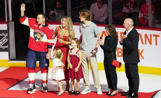 Florida Panthers left wing Brad Marchand, left, waves as he stands with family members as he is recognized for having reached 1,000 NHL points before an NHL hockey game between the Florida Panthers and the Montréal Canadiens, Tuesday, Dec. 30, 2025, in Sunrise, Fla. (AP Photo/Lynne Sladky)