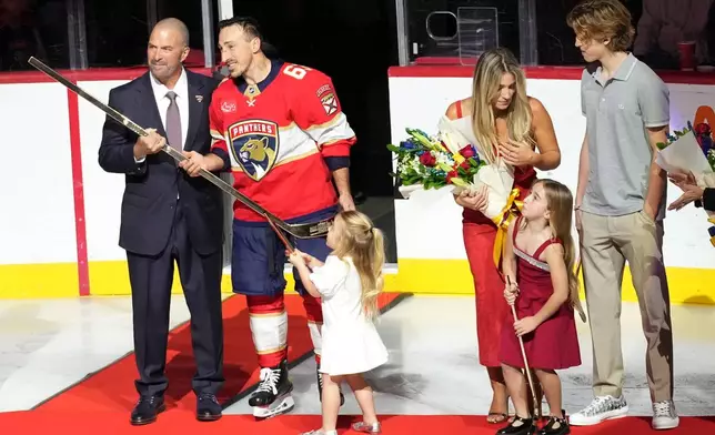 Florida Panthers general manager Bill Zito, left, presents left wing Brad Marchand, second from left, with a golden stick as family members look on as he is recognized for having reached 1,000 NHL points before an NHL hockey game between the Florida Panthers and the Montréal Canadiens, Tuesday, Dec. 30, 2025, in Sunrise, Fla. (AP Photo/Lynne Sladky)