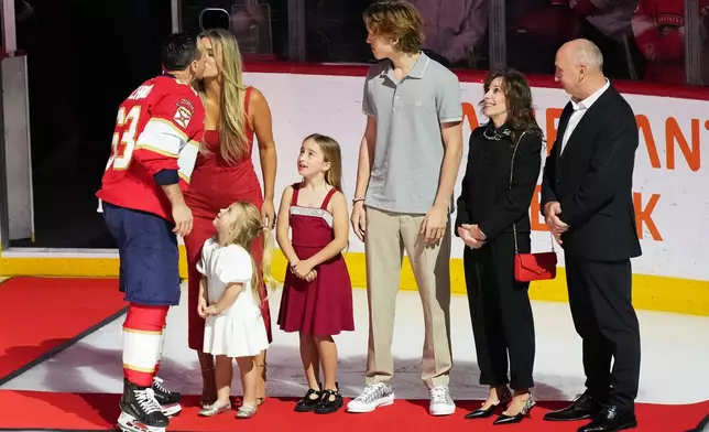 Florida Panthers left wing Brad Marchand, left, kisses his wife Kartrina, second from left, as family members look on as he is recognized for having reached 1,000 NHL points before an NHL hockey game between the Florida Panthers and the Montréal Canadiens, Tuesday, Dec. 30, 2025, in Sunrise, Fla. (AP Photo/Lynne Sladky)