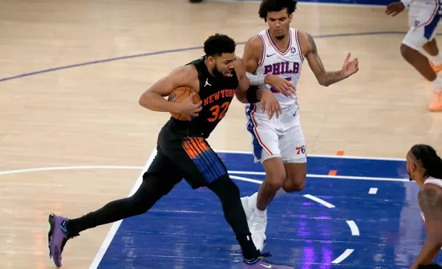 New York Knicks center Karl-Anthony Towns, left, dribbles past Philadelphia 76ers forward Dominick Barlow during the first half of an NBA basketball game, Friday, Dec. 19, 2025, in New York. (AP Photo/John Munson)
