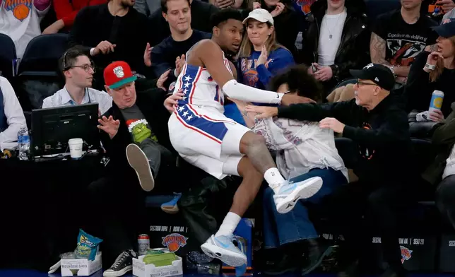 Philadelphia 76ers forward Justin Edwards falls into the lap of former tennis player John McEnroe, left, in red hat, during the first half of an NBA basketball game against the New York Knicks, Friday, Dec. 19, 2025, in New York. (AP Photo/John Munson)