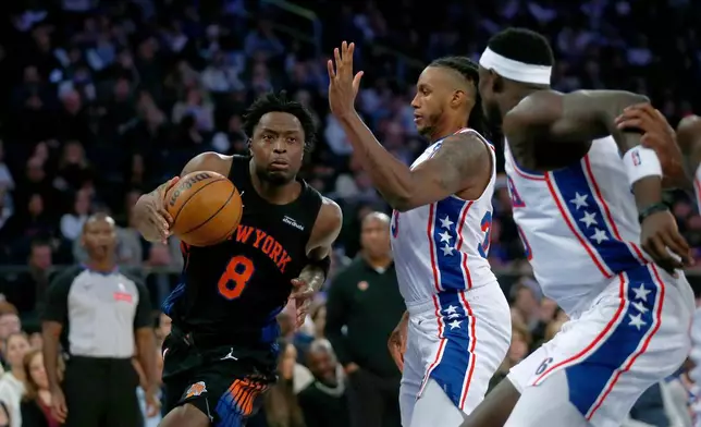 New York Knicks forward OG Anunoby, left, dribbles around Philadelphia 76ers forward Jabari Walker, middle, and center Adam Bona, right, during the first half of an NBA basketball game, Friday, Dec. 19, 2025, in New York. (AP Photo/John Munson)