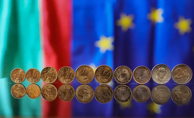 New Euro coins with Bulgarian symbols reflected in a table seen backdropped by Bulgarian and EU flag, Sofia, Tuesday Dec. 30, 2025. (AP Photo/Valentina Petrova)