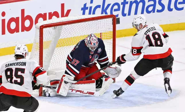 Winnipeg Jets' goaltender Connor Hellebuyck (37) makes a save on Ottawa Senators' Tim Stutzle (18) during the overtime period of their NHL hockey game in Winnipeg, Manitoba, Monday, Dec. 15, 2025. (Fred Greenslade/The Canadian Press via AP)