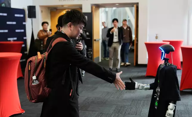 Kochi Sato, left, shakes hands with a humanoid robot during the Humanoids Summit, Thursday, Dec. 11, 2025, in Mountain View, Calif. (AP Photo/Godofredo A. Vásquez)