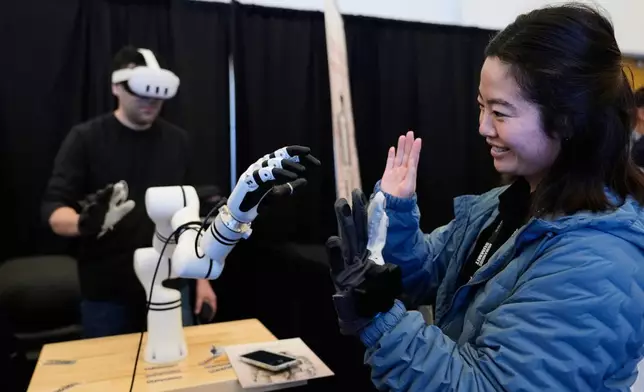 Yuka Iwashita, right, interacts with a robotic hand at the Alt-Bionics table during the Humanoids Summit, Thursday, Dec. 11, 2025, in Mountain View, Calif. (AP Photo/Godofredo A. Vásquez)