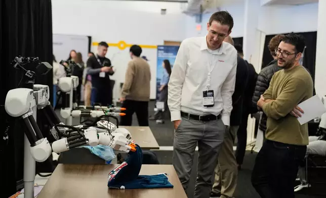 People watch as a robot, made by Weave Robotics, folds clothes during the Humanoids Summit, Thursday, Dec. 11, 2025, in Mountain View, Calif. (AP Photo/Godofredo A. Vásquez)