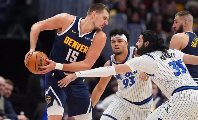 Denver Nuggets center Nikola Jokić, left, looks to pass the ball as Orlando Magic center Goga Bitadze, front right, and guard Noah Penda defend in the first half of an NBA basketball game, Thursday, Dec. 18, 2025, in Denver. (AP Photo/David Zalubowski)