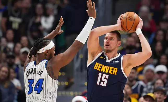Denver Nuggets center Nikola Jokić, right, looks to pass the ball under pressure from Orlando Magic center Wendell Carter Jr. in the first half of an NBA basketball game, Thursday, Dec. 18, 2025, in Denver. (AP Photo/David Zalubowski)