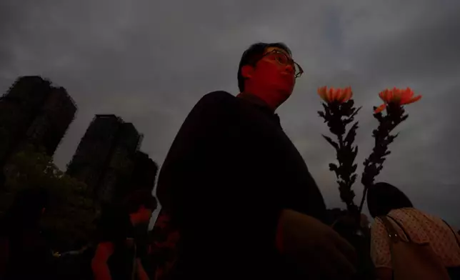 A man holding flowers arrive at the site of a deadly fire at Wang Fuk Court, a residential estate in the Tai Po district of Hong Kong's New Territories, on Tuesday, Dec. 2, 2025. (AP Photo/Ng Han Guan)