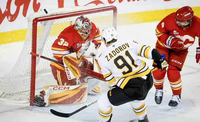Boston Bruins' Nikita Zadorov (91) has his shot deflected by Calgary Flames goalie Dustin Wolf, left, during overtime NHL hockey game action in Calgary, Alberta, Monday, Dec. 29, 2025. (Jeff McIntosh/The Canadian Press via AP)