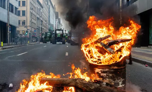 A fire burns in a barrel as European farmers block a road with their tractors during a demonstration outside the EU Summit in Brussels, Thursday, Dec. 18, 2025. (AP Photo/Marius Burgelman)