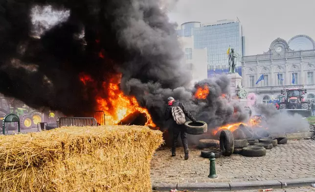 A protestor picks up tire to throw onto a fire during a demonstration of European farmers outside the EU Summit meeting in Brussels, Thursday, Dec. 18, 2025. (AP Photo/Marius Burgelman)