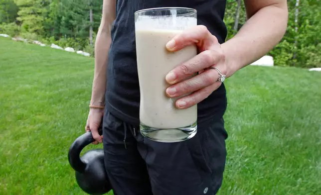 FILE - A woman holds a protein shake and a kettlebell as she poses at her home in Tyngsborough, Mass., on May 15, 2012. (AP Photo/Charles Krupa, File)