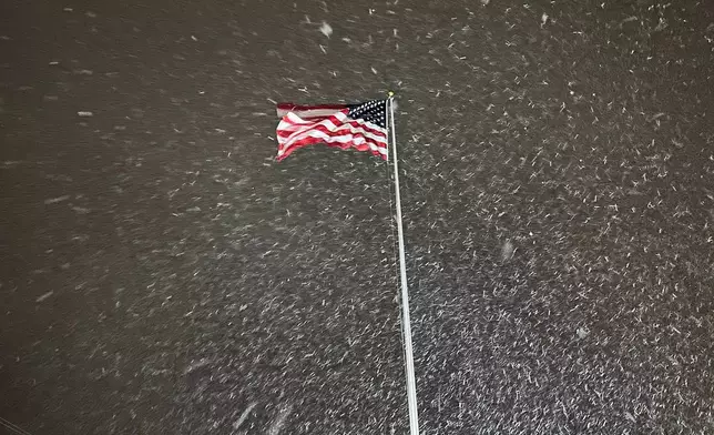 A flag ripples in the wind as snow falls in Lowville, New York, on Tuesday night, Dec. 9, 2025. The area faces a winter storm warning through Thursday. (AP Photo/Cara Anna)