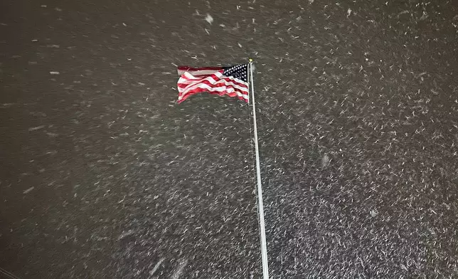 A flag ripples in the wind as snow falls in Lowville, New York, on Tuesday night, Dec. 9, 2025. The area faces a winter storm warning through Thursday. (AP Photo/Cara Anna)