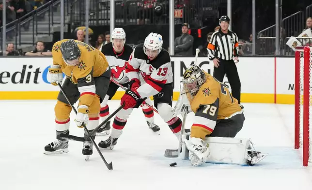 Vegas Golden Knights goaltender Carter Hart (79) stops a shot behind defenseman Brayden McNabb (3) and New Jersey Devils center Nico Hischier (13) during the first period of an NHL hockey game Wednesday, Dec. 17, 2025, in Las Vegas. (AP Photo/Candice Ward)