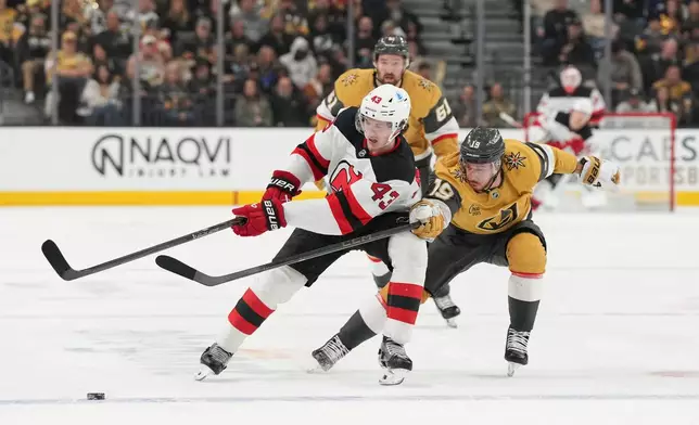New Jersey Devils defenseman Luke Hughes (43) and Vegas Golden Knights right wing Reilly Smith (19) vie for the puck during the first period of an NHL hockey game Wednesday, Dec. 17, 2025, in Las Vegas. (AP Photo/Candice Ward)