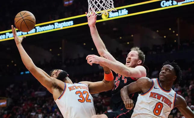 Toronto Raptors' Jakob Poeltl (19) is stopped at the net by New York Knicks' Karl-Anthony Towns (32) and New York Knicks' OG Anunoby (8) during the first half of an NBA Cup basketball game in Toronto, Tuesday, Dec. 9, 2025. (Sammy Kogan/The Canadian Press via AP)