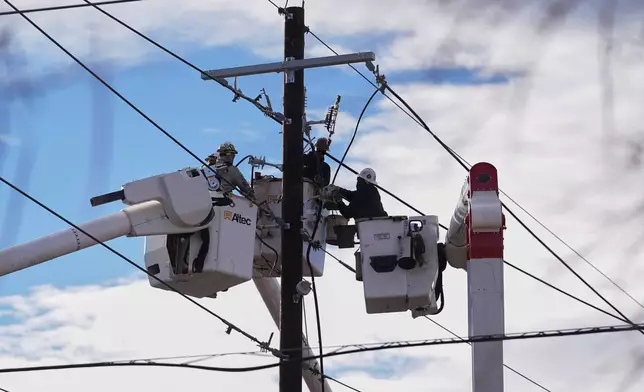 Xcel Energy workers toil to repair power lines on a street closed after hurricane-force winds whipped through the metropolitan area and interrupted service to residents Thursday, Dec. 18, 2025, in Denver. (AP Photo/David Zalubowski)