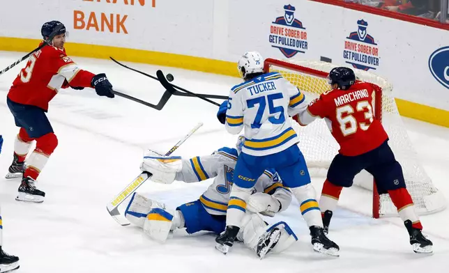 Florida Panthers center Sam Reinhart, left, left wing Brad Marchand (63) and St. Louis Blues defenseman Tyler Tucker (75) try to get control of the puck in front of goaltender Joel Hofer during the second period of an NHL hockey game, Saturday, Dec. 20, 2025, in Sunrise, Fla. (AP Photo/Rhona Wise)