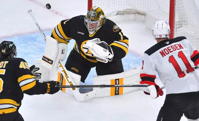 Boston Bruins goaltender Jeremy Swayman (1) deflects the puck as New Jersey Devils right wing Stefan Noesen (11) is unable to score as defenseman Jonathan Aspirot (45) looks on in the second period of an NHL hockey game, Saturday, Dec. 6, 2025, in Boston. (AP Photo/Steven Senne)
