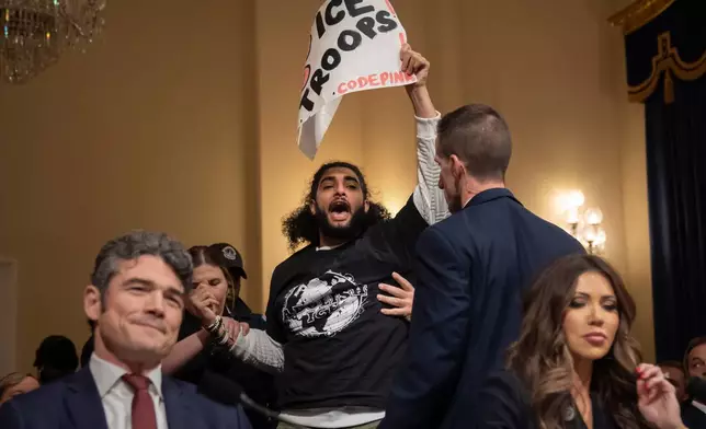 A demonstrator is removed by security officers as Joseph Kent, director of the National Counterterrorism Center, left, and Homeland Security Secretary Kristi Noem sit during a hearing of the House Committee on Homeland Security on Capitol Hill in Washington, Thursday, Dec. 11, 2025. (AP Photo/Mark Schiefelbein)