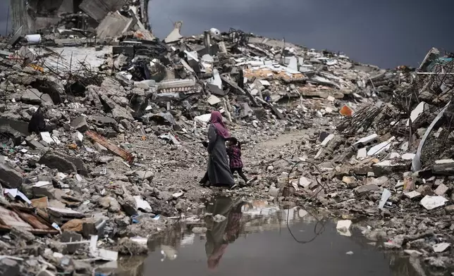 Palestinians walk through the rubble amid stormy weather in Gaza City Thursday, Dec. 11, 2025. (AP Photo/Jehad Alshrafi)