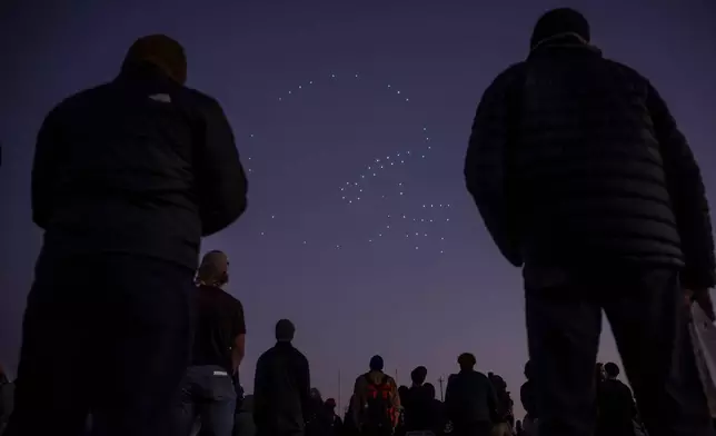 Attendees watch a drone show tribute during a memorial luminaria walk in honor of Laney College football coach John Beam in Oakland, Calif., on Wednesday, Dec. 10, 2025. (Carlos Avila Gonzalez/San Francisco Chronicle via AP)