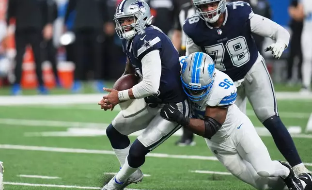 Dallas Cowboys quarterback Dak Prescott, left, tries to hold on to the ball as Detroit Lions defensive end Al-Quadin Muhammad (96) makes a hit during the second half of an NFL football game Thursday, Dec. 4, 2025, in Detroit. (AP Photo/Paul Sancya)