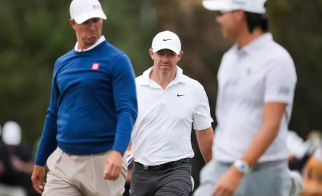 Rory McIlroy of Northern Ireland (centre) reacts after completing his round with Adam Scott of Australia (Left) and Min Woo Lee of Australia (Right) during the first round of the Australian Open golf tournament in Melbourne, Australia, Thursday, Dec. 4, 2025. (AP Photo/Asanka Brendon Ratnayake)