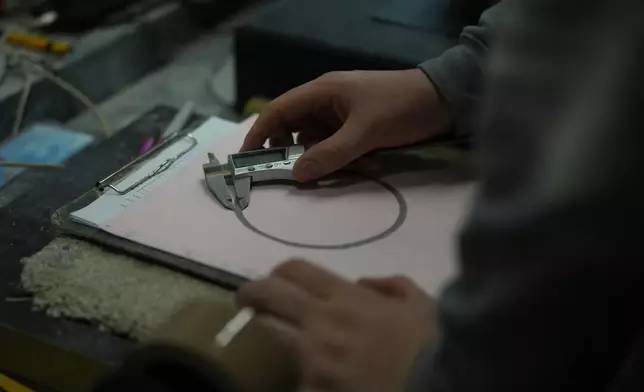 A craftsman uses calipers to measure the amount of a curling sone that has contact with the ice, during a quality control phase at Kays Curling stone factory in Mauchline, Scotland, Tuesday, Nov. 11, 2025. (AP Photo/Alastair Grant,)