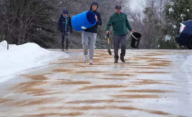 Chase Caruso, center, and his father, Peter Caruso, spread sand on their icy driveway during a freezing rainstorm, Monday, Dec. 29, 2025, in Harrison, Maine. (AP Photo/Robert F. Bukaty)